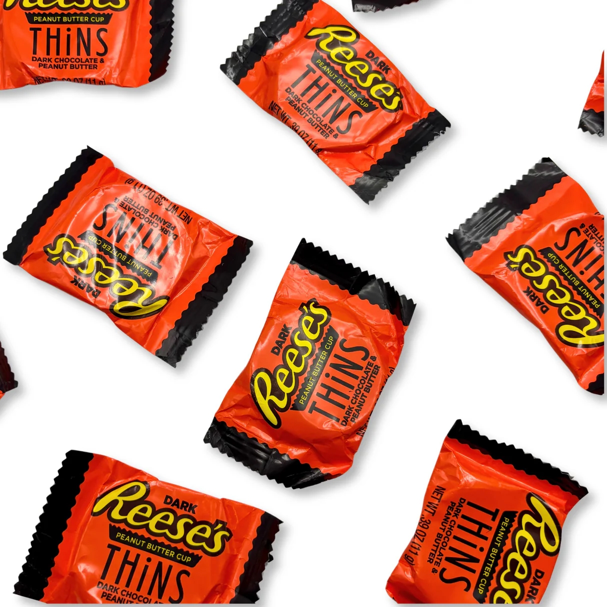 Dark chocolate Reese's Thins Peanut Butter Cups in orange wrappers with black accents scattered on a white background.