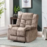 A plush beige recliner with a padded back and armrests is placed on a patterned rug in a cozy room, featuring a small wooden table with decorative items and plants nearby.