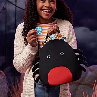 Young girl smiling, holding a lollipop and a plush spider with a simple face and red belly.