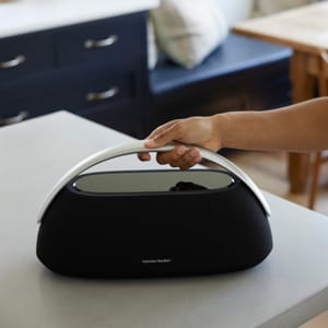 A person is holding a sleek, curved portable speaker with the logo Harman/Kardon on it.