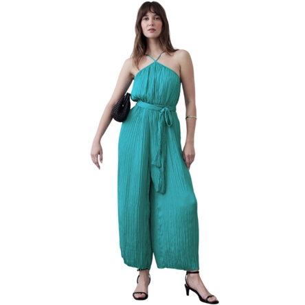 A woman wears a teal, halter-neck, sleeveless jumpsuit with a pleated texture and a waist tie. She accessorizes with a black bag and black heeled sandals.
