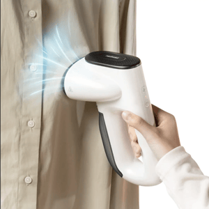 A handheld garment steamer is being used to remove wrinkles from a shirt, with visible steam emitted from the nozzle.