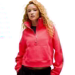 A woman wears a bright pink oversized scuba half-zip pullover with a funnel neck and a front kangaroo pocket. The design is casual and comfortable, paired with black pants.