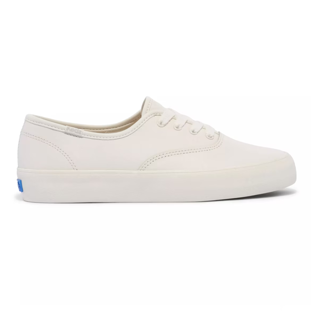 A classic white canvas sneaker with a low-top design, featuring a simple lace-up closure and a small blue tag on the back heel.