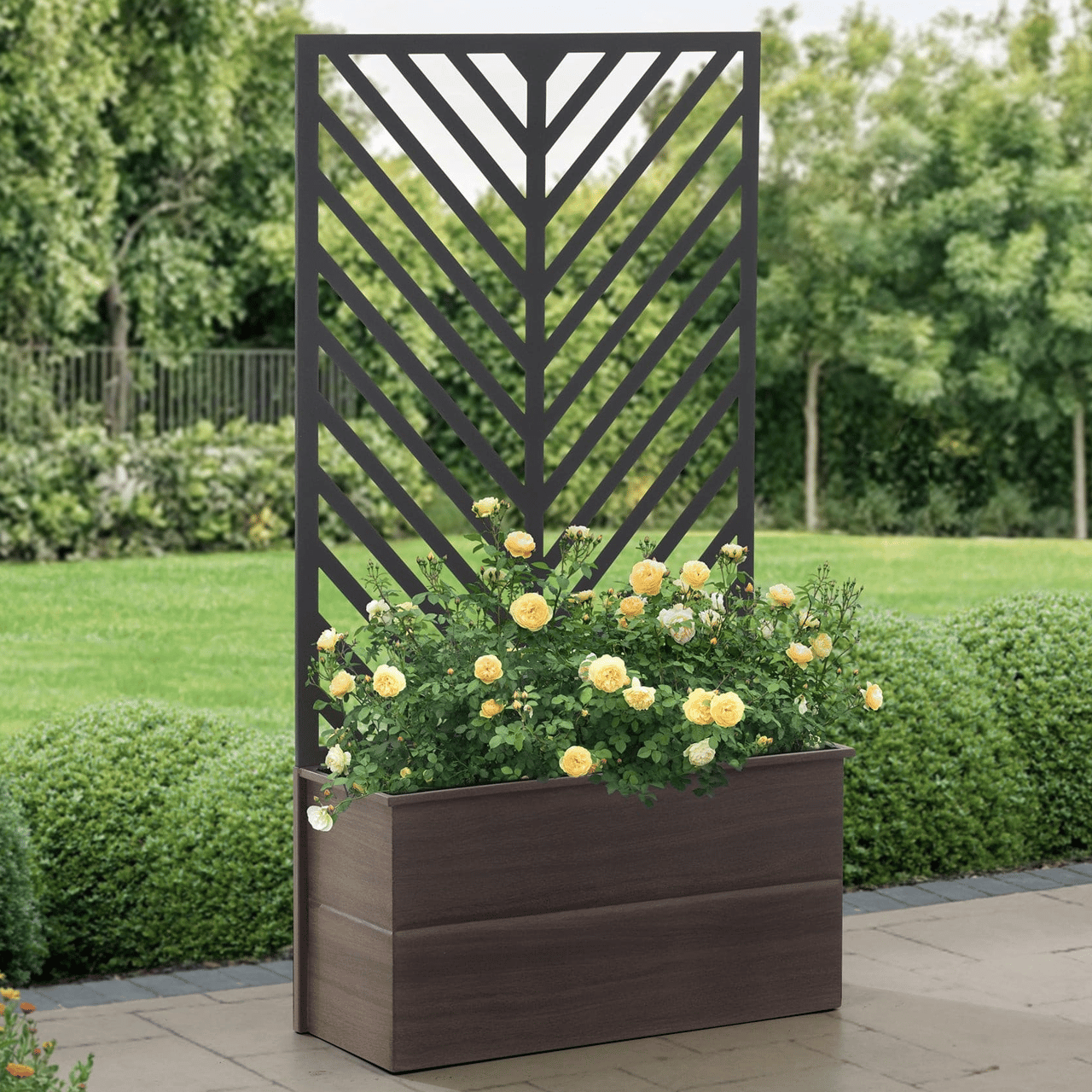 A wooden raised garden bed features a geometric trellis backing, housing flowering yellow roses. It stands on a paved area surrounded by lush green gardens and trees.