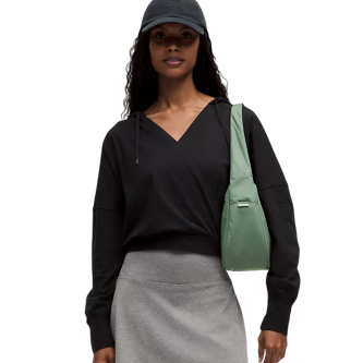 A person wearing a black hoodie and gray skirt is carrying a light green shoulder bag and wearing a dark cap.