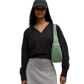 A person wearing a black hoodie and gray skirt is carrying a light green shoulder bag and wearing a dark cap.