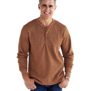 A man wears a brown long-sleeve henley shirt with a ribbed texture and blue jeans.