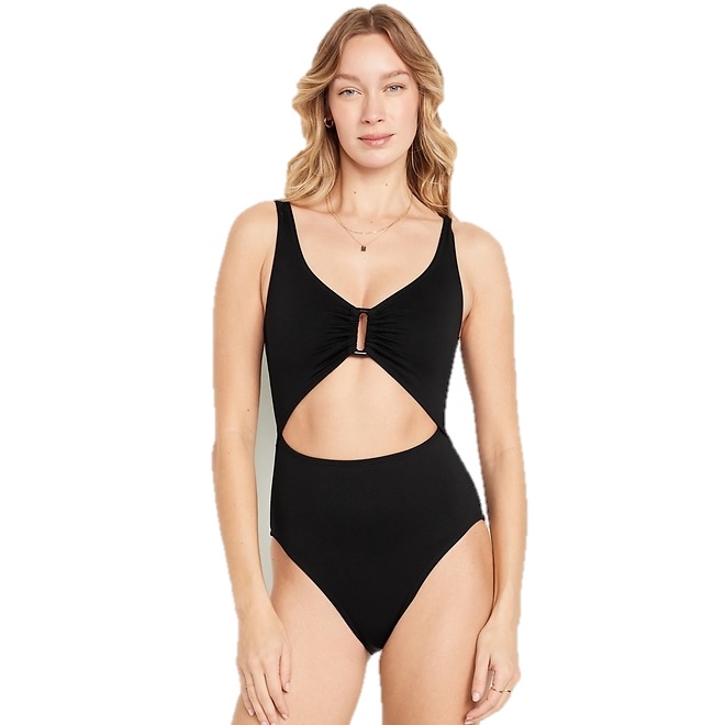 A woman is wearing a black cut-out one-piece swimsuit with a keyhole and ruching detail at the front.