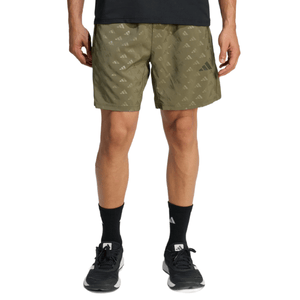 A person wearing olive green shorts with an all-over logo pattern, black socks, and black athletic shoes.