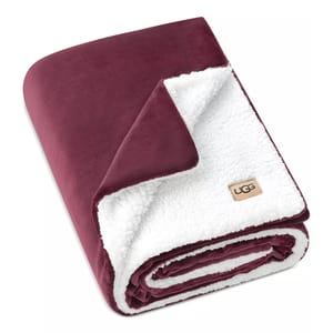A maroon and white UGG blanket featuring a plush, velvety exterior and a soft sherpa interior.