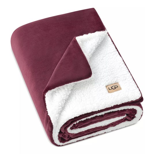 A maroon and white UGG blanket featuring a plush, velvety exterior and a soft sherpa interior.