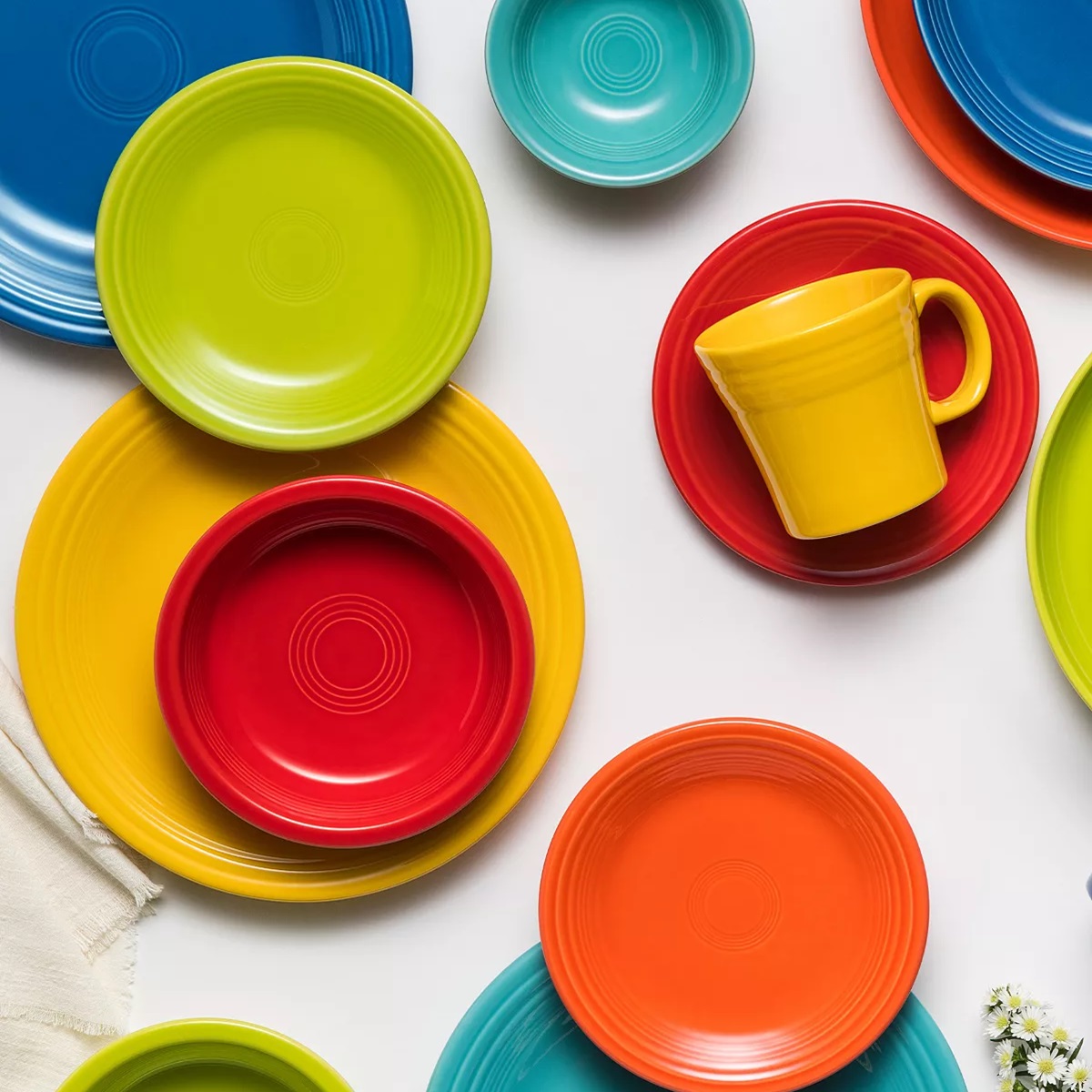 Colorful ceramic dinnerware including plates in blue, green, yellow, and red, and a yellow cup.