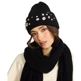 A woman is wearing a black beanie adorned with rhinestones and a matching black scarf over a cream top.