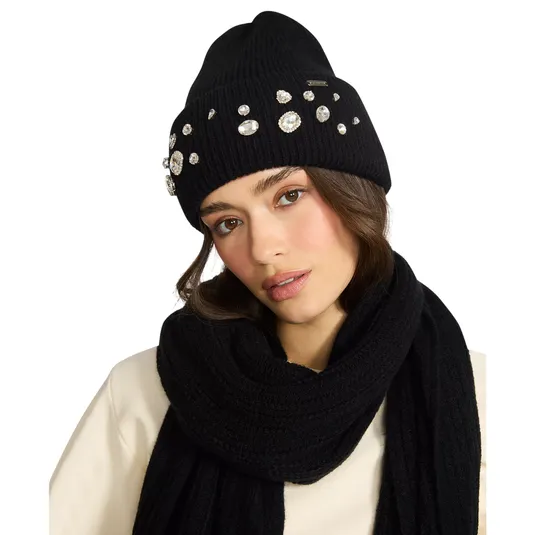 A woman is wearing a black beanie adorned with rhinestones and a matching black scarf over a cream top.