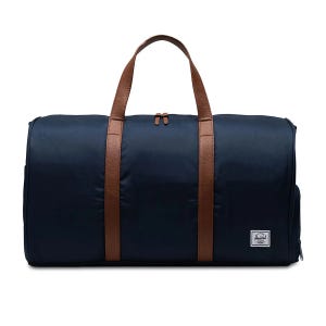 A navy duffel bag features brown handles and a zipper closure, with a small white logo patch on the front.