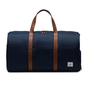 A navy duffel bag features brown handles and a zipper closure, with a small white logo patch on the front.