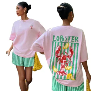 A woman wearing a light pink T-shirt with a lobster and lemon design, paired with green striped shorts and holding a yellow netted bag.