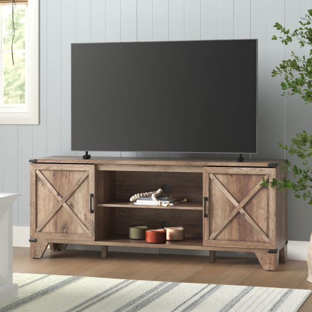A flat-screen TV sits atop a rustic wooden console with barn-style sliding doors and open shelving, set against a paneled wall.