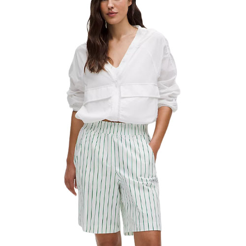 A person is wearing a white blouse with long sleeves and a deep V-neck paired with high-waisted, knee-length white shorts featuring thin vertical green stripes.