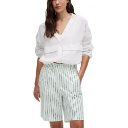 A person is wearing a white blouse with long sleeves and a deep V-neck paired with high-waisted, knee-length white shorts featuring thin vertical green stripes.