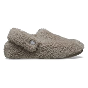 Crocs Cozzzy Slippers feature a plush, fuzzy exterior in a beige color with a rounded toe and a slip-on design, including a small circular logo detail on the side.