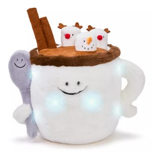 A plush toy designed to resemble a smiling mug of hot chocolate, featuring decorative marshmallows with reindeer antlers and a snowman face on top, two cinnamon sticks, and a spoon with a happy face.