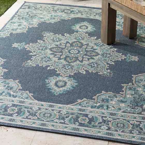 Blue and teal area rug with an intricate floral medallion pattern and decorative border, placed partially under a wooden bench.