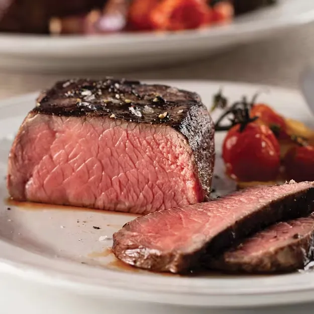 A medium-rare steak is sliced on a plate, garnished with flaky salt. Roasted cherry tomatoes are served alongside.