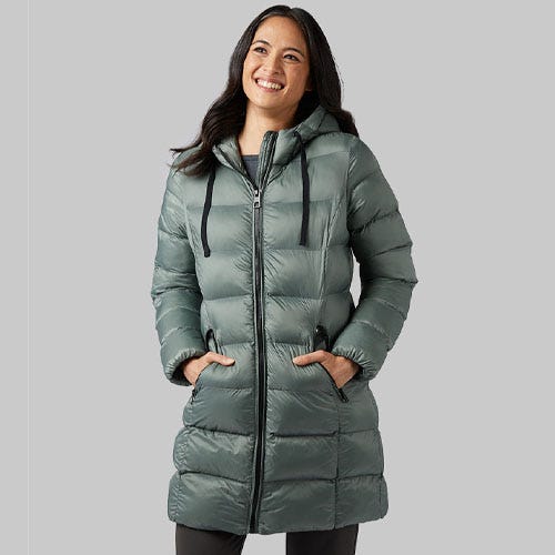 a woman with dark hair wearing a sage green 3/4 length puffer coat against a grey background