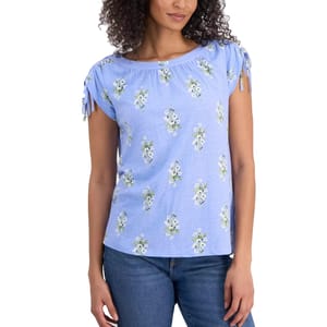 Blue floral short-sleeve top with gathered neckline and drawstring details on the sleeves, paired with blue jeans.