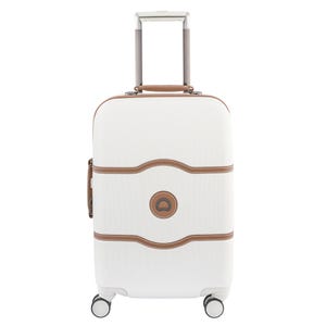 Delsey Paris Chatelet Carry-On features a white hard shell with brown trim, four spinner wheels, and a telescopic handle, designed for easy maneuverability.