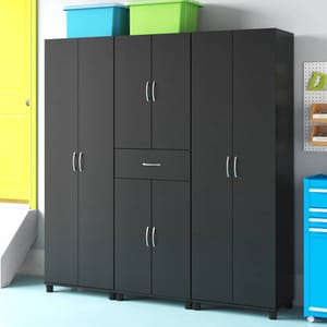 A black garage storage system featuring multiple cabinets and a drawer, with silver handles on elevated feet. Two storage bins are placed on top, and a pegboard with tools is visible nearby.