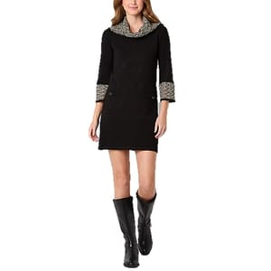 A woman in a black dress with patterned collar and cuffs walks wearing knee-high black boots.