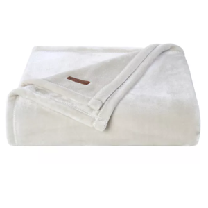 A folded, cream-colored Columbia Plush Throw featuring a soft, velvety texture with a small brown logo patch on the corner.