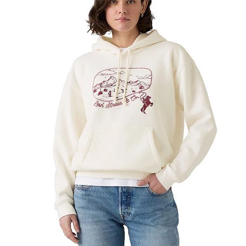 A person wears a cream-colored hoodie with a red graphic and text, paired with blue jeans.