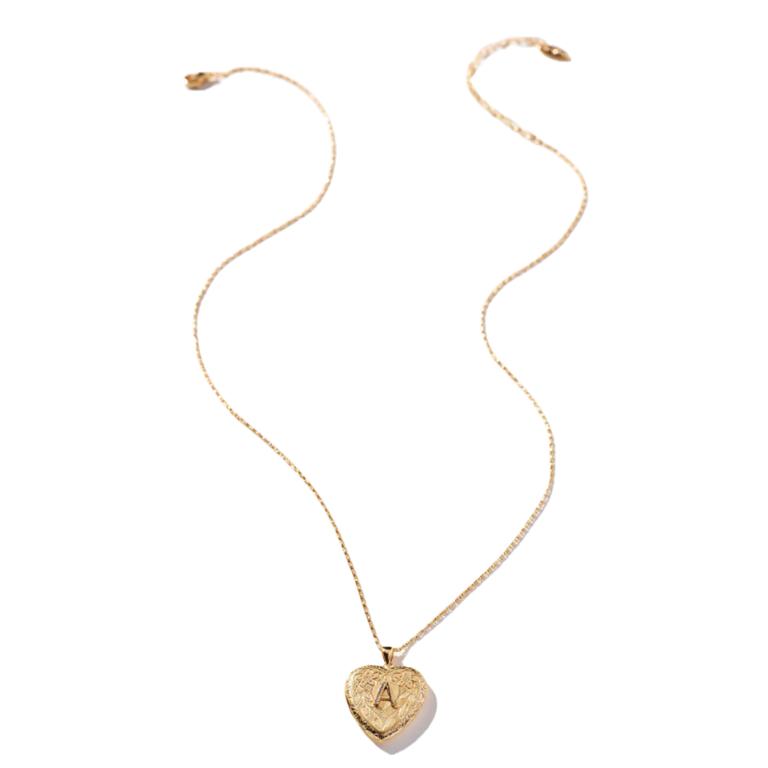 A gold heart-shaped locket necklace with a textured surface and a prominent \“A\“ monogram. The chain is thin and elegant, complementing the locket's design.