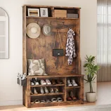 A rustic wooden entryway bench with shoe storage, hooks for hats and coats, and upper cubbies for additional storage. Accessories include shoes, hats, a bag, an umbrella holder, and a decorative plant.