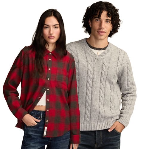 A woman in a red and black plaid shirt stands next to a man wearing a light gray cable-knit sweater. Both are dressed casually.
