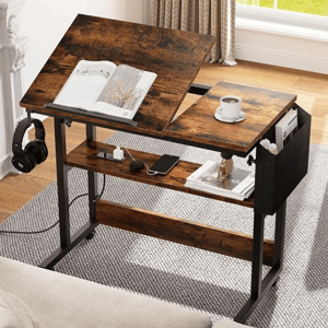 A rustic brown adjustable drawing table with storage shelves, a side pocket, and a hook for headphones. It contains a book, coffee cup, smartphone, and charger on top, and has a neutral carpet and sofa nearby.