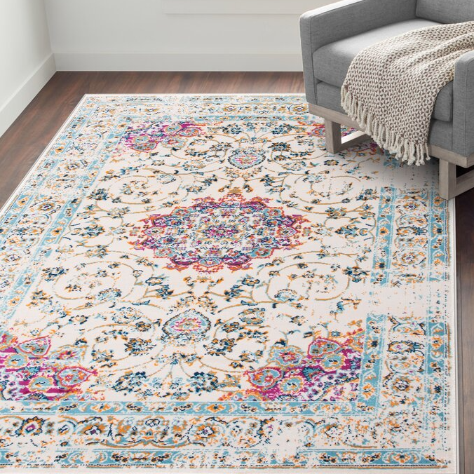 A 5' x 7' area rug with a stain-resistant finish, featuring an intricate floral and geometric pattern with vibrant colors including pink, blue, and orange on a light background.