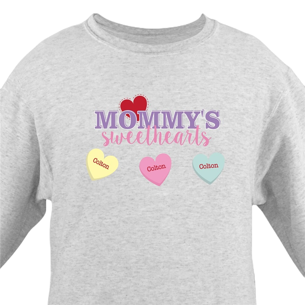 A gray sweatshirt features \“Mommy's Sweethearts\“ in purple and pink text, with three candy heart illustrations underneath, each labeled \“Colton\“ in red text on yellow, pink, and blue hearts.