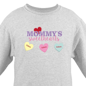 A gray sweatshirt features \“Mommy's Sweethearts\“ in purple and pink text, with three candy heart illustrations underneath, each labeled \“Colton\“ in red text on yellow, pink, and blue hearts.