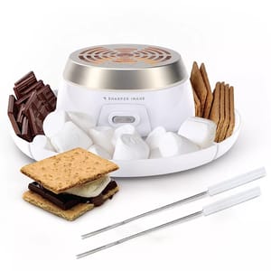 A Sharper Image S'mores Maker featuring an electric heater for roasting marshmallows, surrounded by compartments for chocolate and graham crackers, includes two roasting sticks and an on-off switch.
