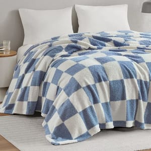 A blue and white checkered blanket is draped over a bed with two white pillows. A small wooden side table with a glass of water is beside the bed.
