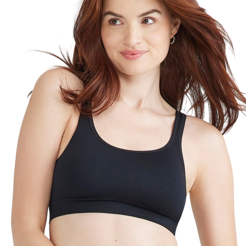 A woman is wearing a black sports bra and beige high-waisted underwear.