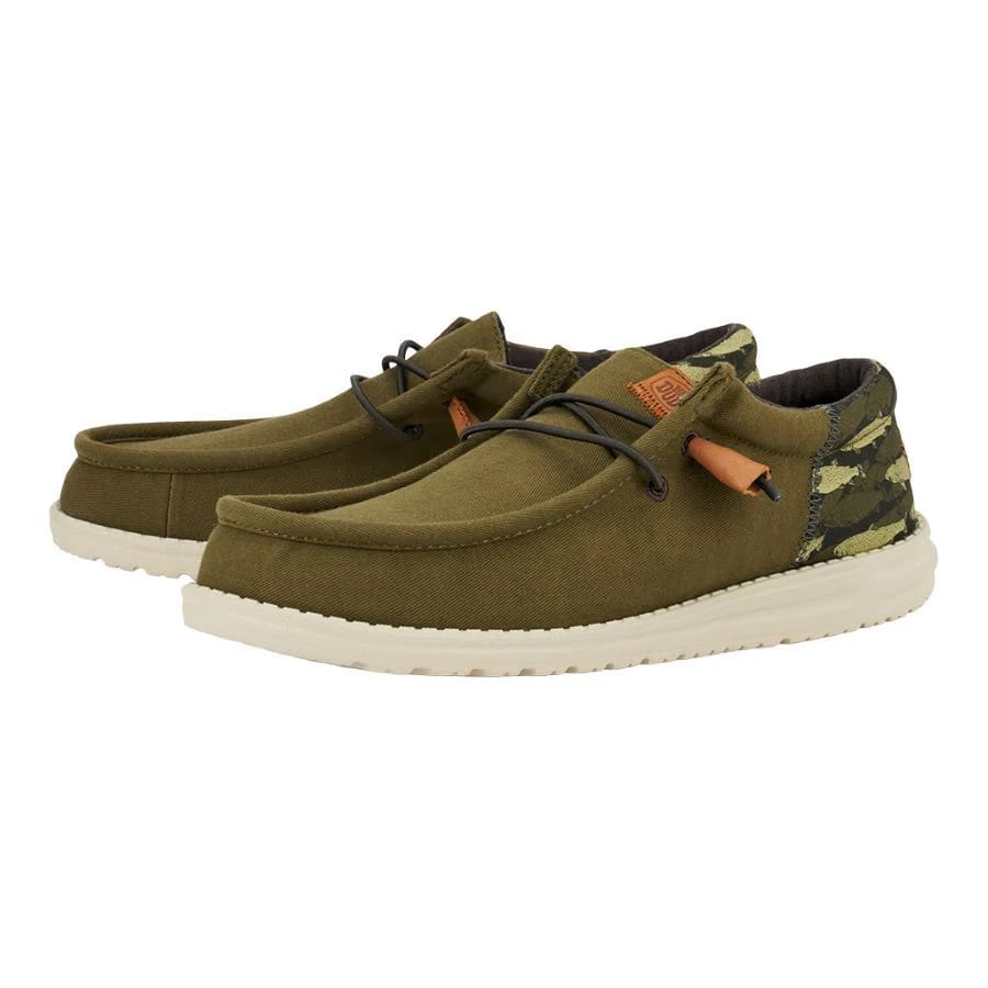 A pair of olive green canvas shoes with a white sole and camouflage details at the heel.