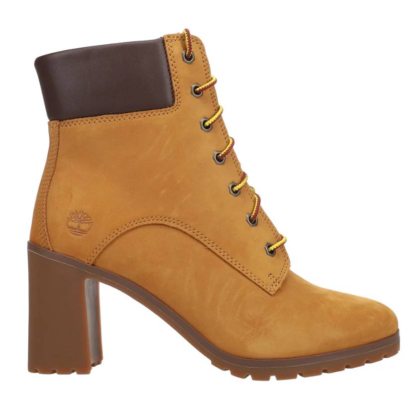 A tan, high-heeled ankle boot with yellow laces, featuring a padded dark brown collar and rubber lug sole, embossed with the Timberland logo.