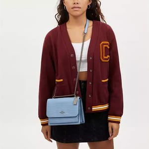 A woman wearing a varsity jacket, a crop top, a dark mini skirt, and carrying a light blue shoulder bag.