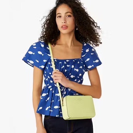 A woman is wearing a blue blouse with a white cloud pattern and holding a pale green crossbody bag.